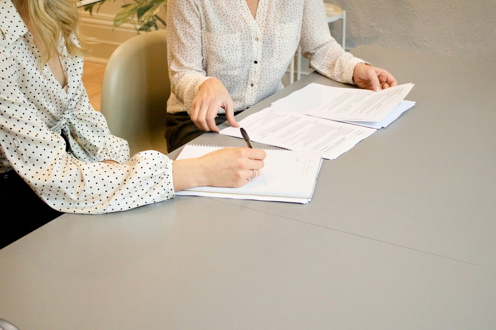 woman signing on white printer paper beside woman about to touch the documents, commercial & personal
